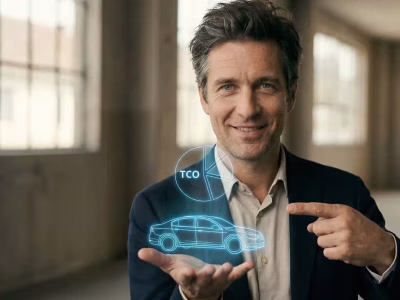 A man in a navy blazer presenting a futuristic blue holographic display. The hologram features a wireframe of a car and a pie chart labeled "TCO," illustrating the use of Fleetwaro.ai and AI for automated invoice processing and fleet cost management.